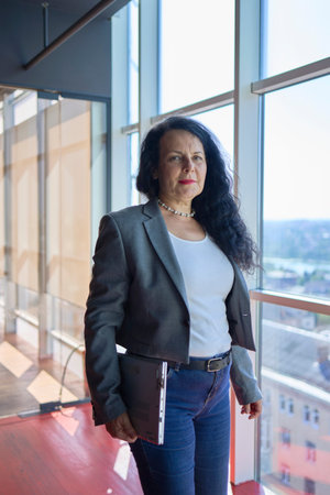 57-year-old woman walks with a laptop to her glass office in a modern workspace