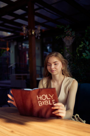 a beautiful teenage girl in a peach fluffy suit with a waistcoat in the old money  style reads the Holy Bible and praysの写真素材
