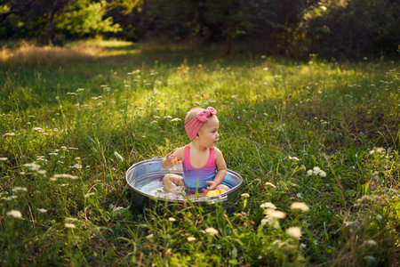 a baby in a metal tub plays with rubber ducklings in the summer gardenの写真素材