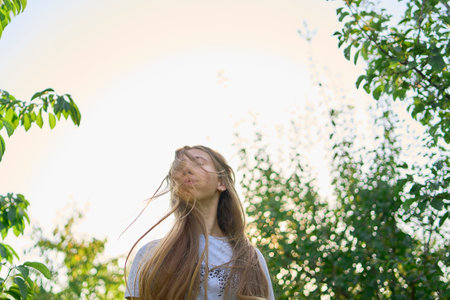 portrait of a teenage girl with long blond hair in a sunlit gardenの写真素材