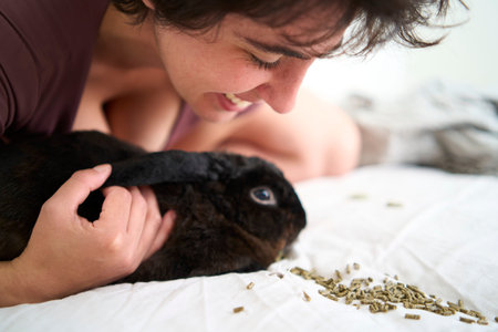 a  young plus size woman in home clothes playing with her pet rabbit on bed in student dormitoryの写真素材
