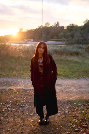 15-year-old teenage girl in a black long coat at sunset by the river