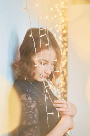 teenage girl in a dress surrounded by golden Christmas lightsの写真素材