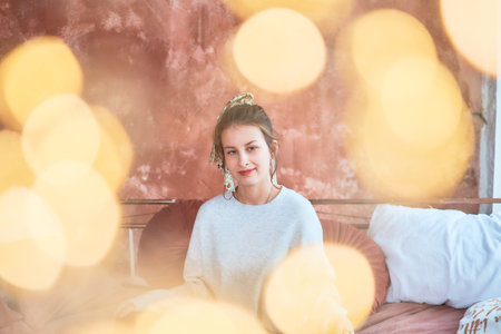 teenage girl in bed hugging pillows surrounded by golden Christmas lights