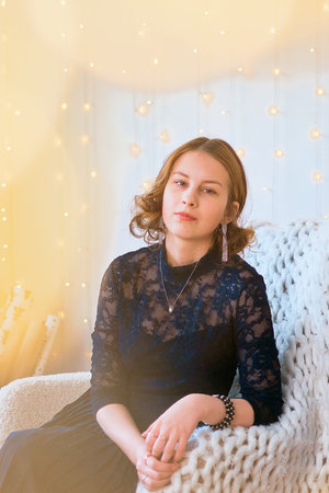 a teenage girl in a dress near an unconventional Christmas tree surrounded by golden lights