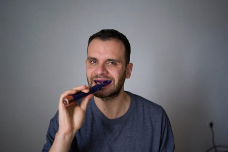 30-year-old man brushes his teeth with purple toothpaste using an electric toothbrush