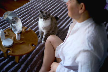Person relaxing on bed with cats and beauty products on wooden trayの写真素材