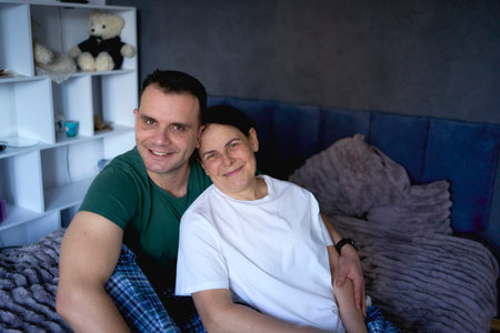 two people sitting together on a bed with stuffed toys visible on shelves in background