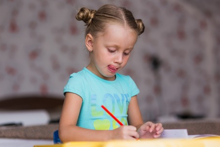 Girl learns lessons carefully. She writes in a notebook with a pencil.の写真素材