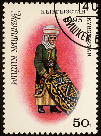 Moscow, Russia - August 07, 2017: A stamp printed in Kyrgyzstan, shows woman in traditional Kyrgyz costume with carpet, seriesのeditorial素材