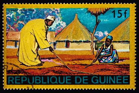 Moscow, Russia - February 27, 2018: stamp printed in Guinea shows African village, man and woman are cultivating a field, Guinean forest region, series "Regional Costumes and Habitations", circa 1968のeditorial素材