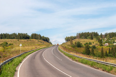 Highway through hills covered with meadows and green forest, sunny summer dayの写真素材