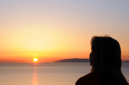 Silhouette profile of a woman looking at the sun rising from the seaの写真素材