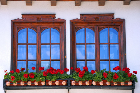 Two windows decorated with potted red flowers in Bulgariaの写真素材