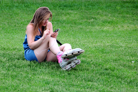 MOSCOW, RUSSIA - MAY 31, 2015: Roller skate girl sits on the lawn in the park and dials a telephone numberのeditorial素材
