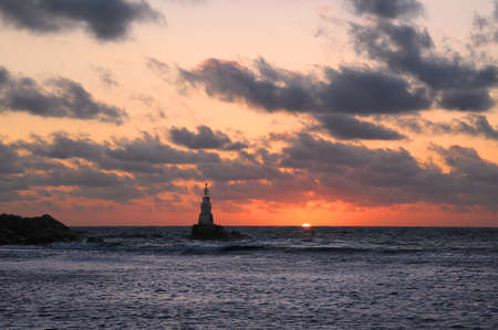 Tiny lighthouse, dark rocks and sea in the town of Akhtopol in Bulgaria at sunriseの写真素材