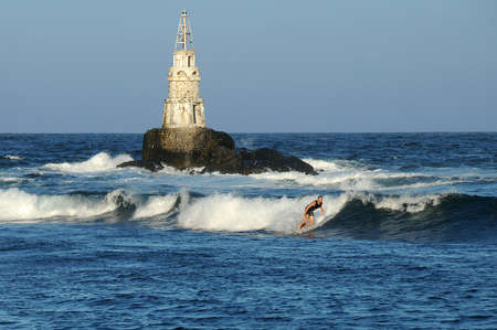 AKHTOPOL, BULGARIA - SEPTEMBER 16, 2020: Unidentified young surfer surfs waves in the Black sea near tiny lighthouseのeditorial素材