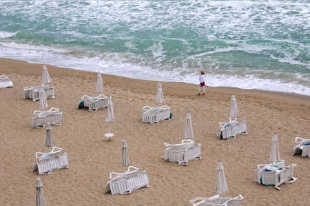 OBZOR, BULGARIA - JUNE 16, 2021: Unidentified Caucasian woman wearing white clothes walks along the beach on a windy day during low seasonのeditorial素材