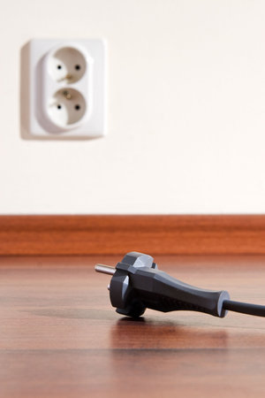Two pin plug on the floor and electrical outlet in background