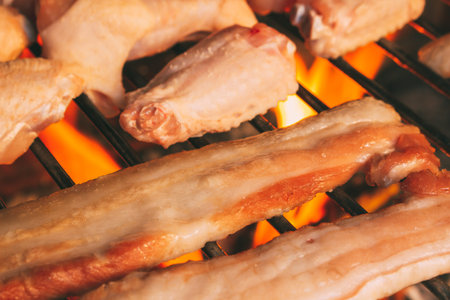 Bacon and chicken wings prepared on the grill during a barbecueの写真素材