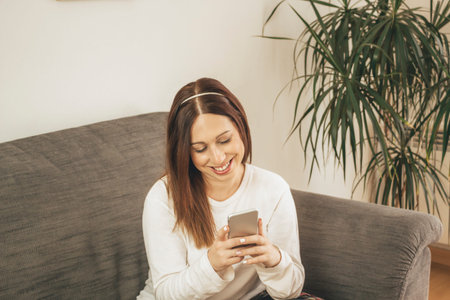 Young brown-haired woman using her smartphone from her home coach while resting
