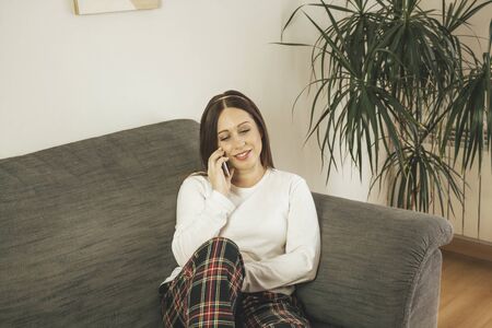 Young brown-haired woman using her smartphone from her home coach while restingの写真素材