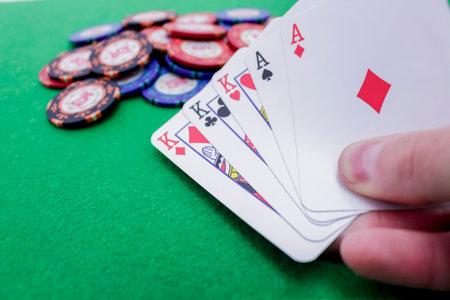 Hand holding five playing cards, three kings and two aces on poker chips on a green table