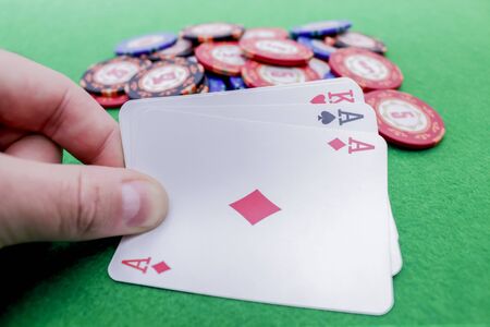 Hand holding  playing cards with two aces and one king on poker chips on a green tableの写真素材
