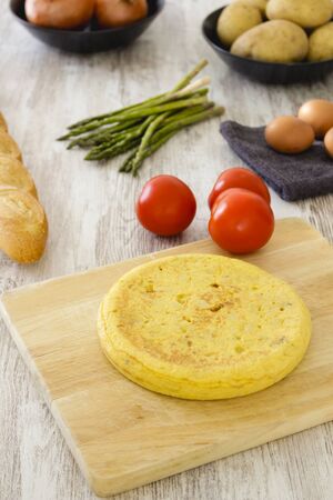 Potato omelette as a typical Spanish dish along with different healthy and vegetarian ingredients such as tomatoes, onions, eggs or asparagus, accompanied by a handmade loaf of bread, selective focus.の写真素材