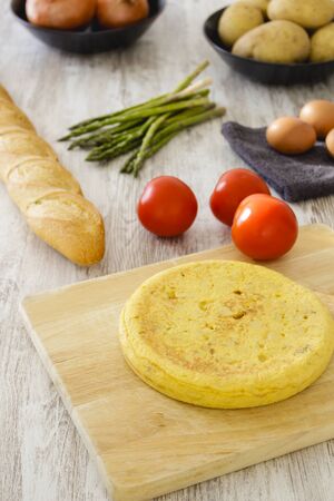 Potato omelette as a typical Spanish dish along with different healthy and vegetarian ingredients such as tomatoes, onions, eggs or asparagus, accompanied by a handmade loaf of bread, selective focus.の写真素材
