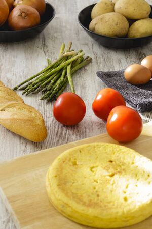 Potato omelette as a typical Spanish dish along with different healthy and vegetarian ingredients such as tomatoes, onions, eggs or asparagus, accompanied by a handmade loaf of bread, selective focus.の写真素材
