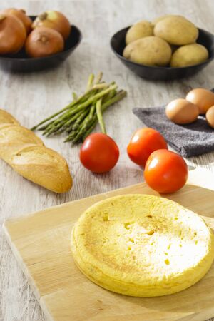 Potato omelette as a typical Spanish dish along with different healthy and vegetarian ingredients such as tomatoes, onions, eggs or asparagus, accompanied by a handmade loaf of bread, selective focus.の写真素材