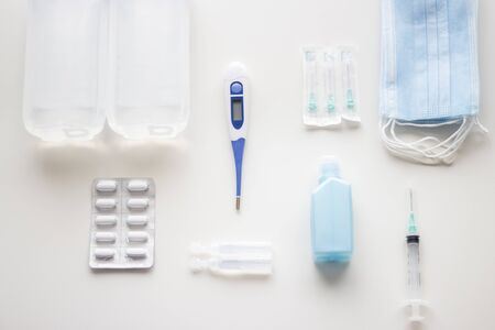 Medical supplies kit for health emergencies, consisting of thermometer, bandages, analgesics, antiseptics, serum, hand sanitizer, needles and syringe or masks on white background, selective focusの写真素材