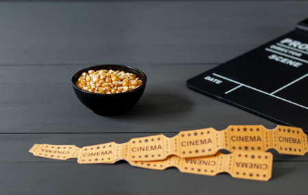 Bowl with corn kernels, to prepare popcorns, next to a clapperboard and some movie tickets, on a...
