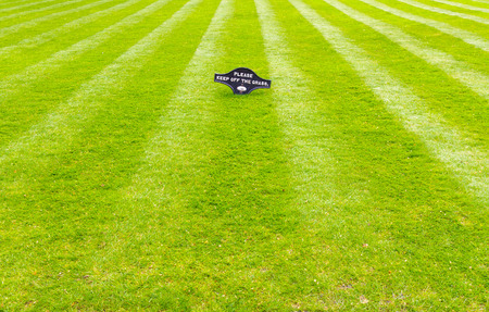 A beautiful green garden lawn that has just been mowed with an attractive pattern of stripes and a sign of Please Keep Off The Grassの写真素材