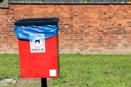 Red dog waste bin against a brick wallの写真素材