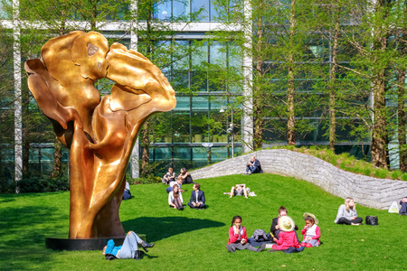 London, UK - May 10, 2017 - Fortuna, a bronze sculpture by Helaine Blumenfeld in Jubilee Park, Canary Wharf, where people are sitting and relaxing on the green grass during a sunny dayのeditorial素材