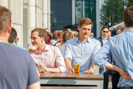 London, UK - May 10, 2017 - A young businessman drinking with his colleagues at a packed outdoor bar in Canary Wharf on a sunny dayのeditorial素材