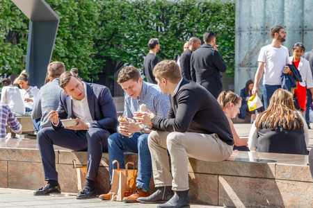 London, UK - May 10, 2017 - Three businessmen on their lunch break in Cabot Square, Canary Wharf packed with people eating and chatting on a sunny dayのeditorial素材