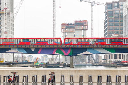 Light train passing through Canary Wharf in London with new development construction site in the...