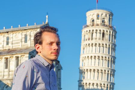 A white young man poses in front of the Leaning Tower in Pisa, Italyの写真素材