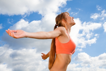 smiling young woman with hands up on the sky backgroundの写真素材