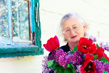 portrait of an elderly woman with flowers in the spring gardenの写真素材