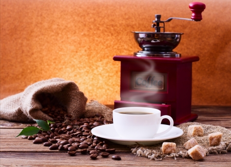 Cup of Warm Coffee, Sugar and Grinder. Coffee Beans scattered on Wooden Surface. Free space for your Textの写真素材