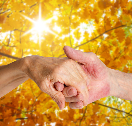 Old people holding hands closeup. Background on sunny autumn landscapeの写真素材