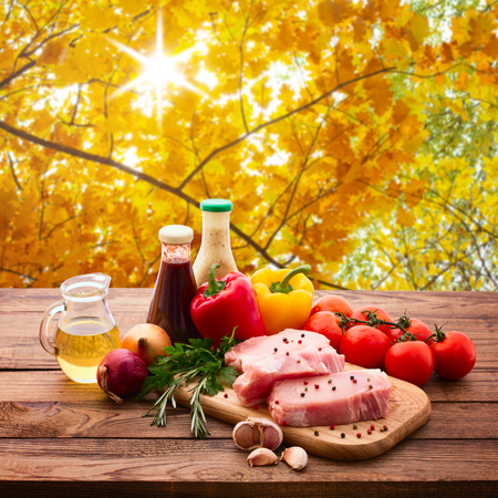 Food. Raw meat for barbecue with fresh vegetables and mushrooms on wooden surface. Tomatoes, peppers, spices for cooking meat. Autumn landscape. Collage.の写真素材