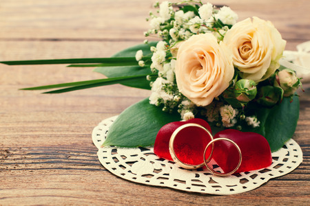 Bridal bouquet of white flowers on wooden surface. Summer wedding day, unusual designer florist bouquet of delicate roses. Wedding rings. Free space for text.の写真素材