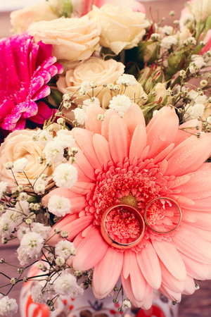 Bridal bouquet of white flowers on wooden surface. Summer wedding day, unusual designer florist bouquet of delicate roses. Wedding rings. Free space for text.の写真素材