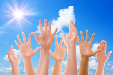 Raised up hands of many people on background of blue sunny sky closeupの写真素材