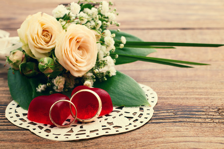 Bridal bouquet of white flowers on wooden surface. Wedding day, unusual designer florist bouquet of delicate roses. Wedding rings.の写真素材